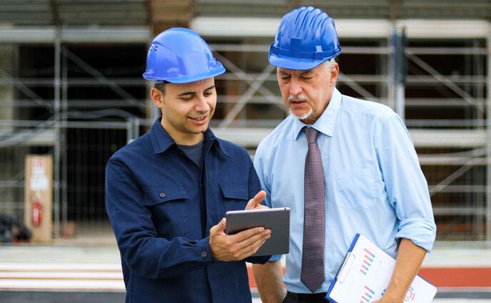Facility maintenance plan two managers reviewing building plans construction site using tablet