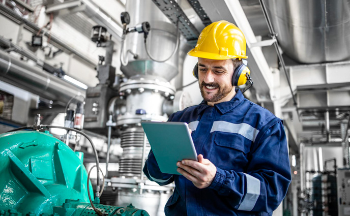 cmms software features industrial engineer standing by gas generator with tablet