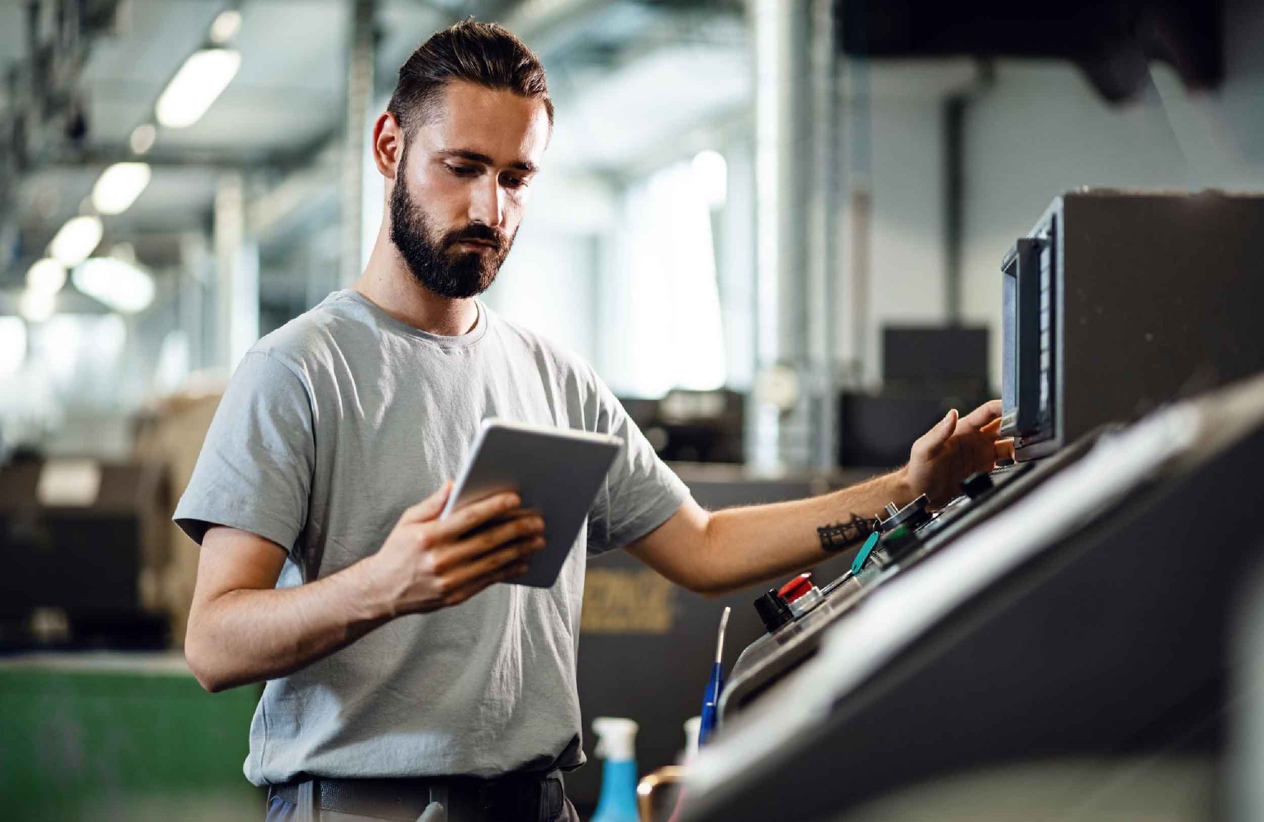 equipment maintenance software young worker operating cnc machine while using digital tablet industrial facility